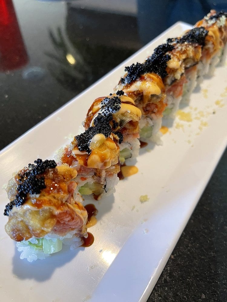 A row of sushi roll pieces topped with black tobiko, spicy mayo and eel sauce on a long white plate