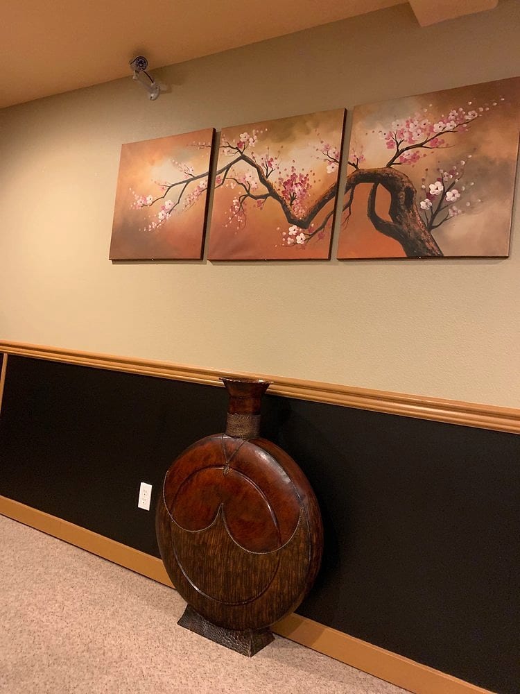 A three-panel cherry blossom painting above a large carved wooden vase in the dining room