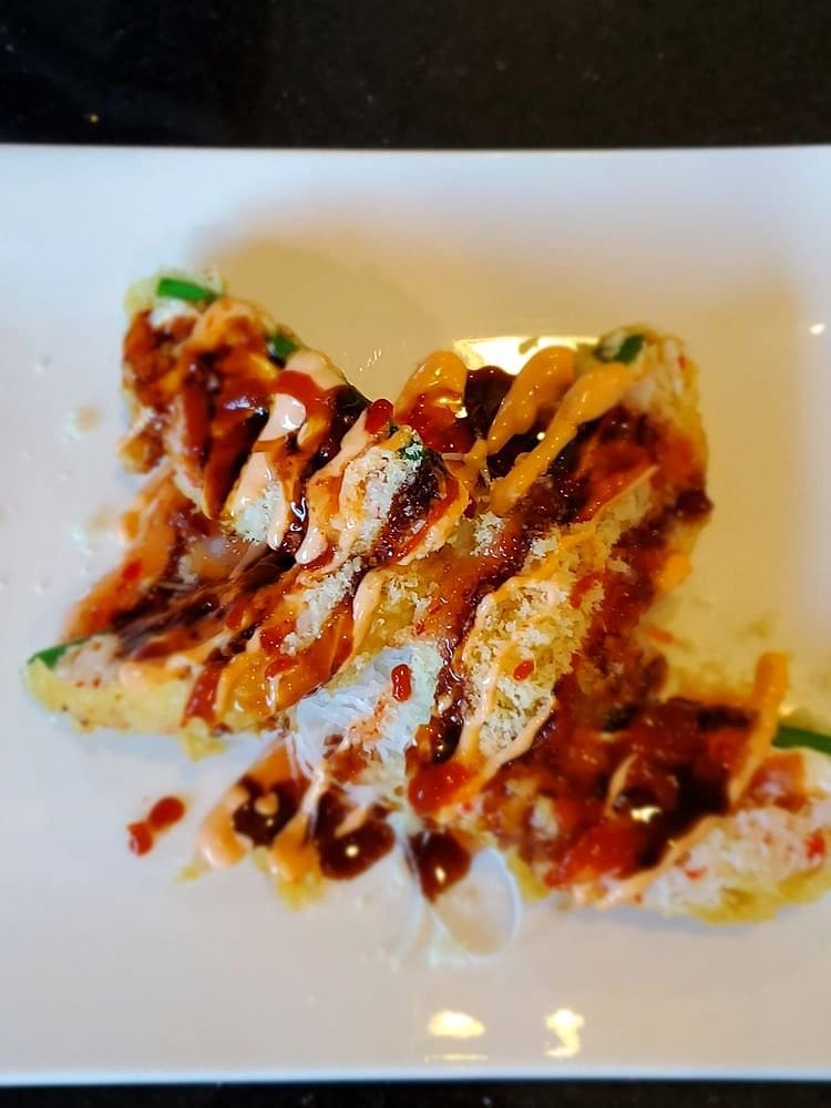 Crispy fried roll pieces drizzled with spicy mayo, eel sauce and chili on a white plate