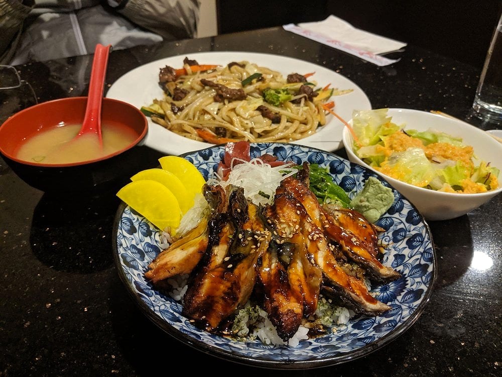 A glazed eel bowl with pickled radish and wasabi, served with miso soup, a green salad and a plate of yakisoba