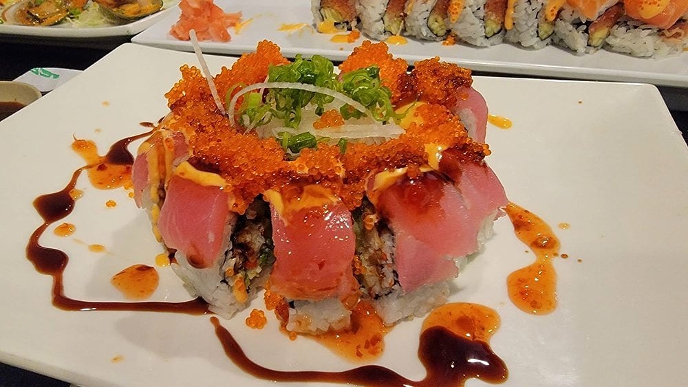 A roll wrapped in tuna and crowned with orange tobiko and green onion, swirled with eel sauce and chili sauce