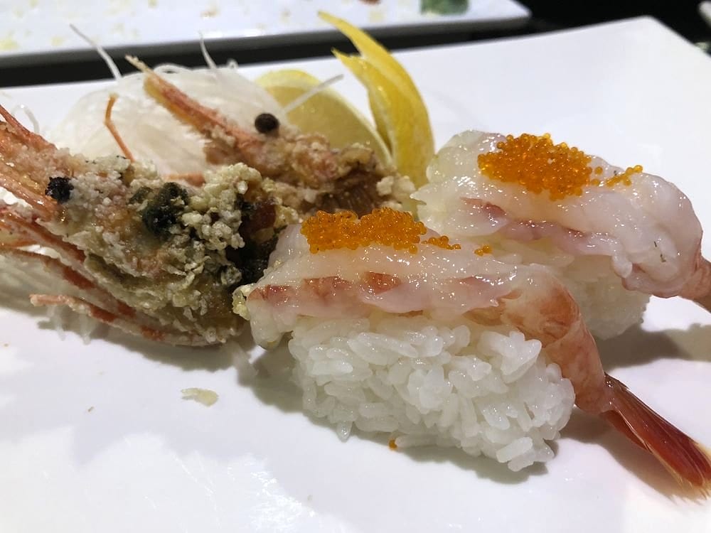 Sweet shrimp nigiri topped with orange tobiko, with the fried shrimp heads and a lemon wedge alongside