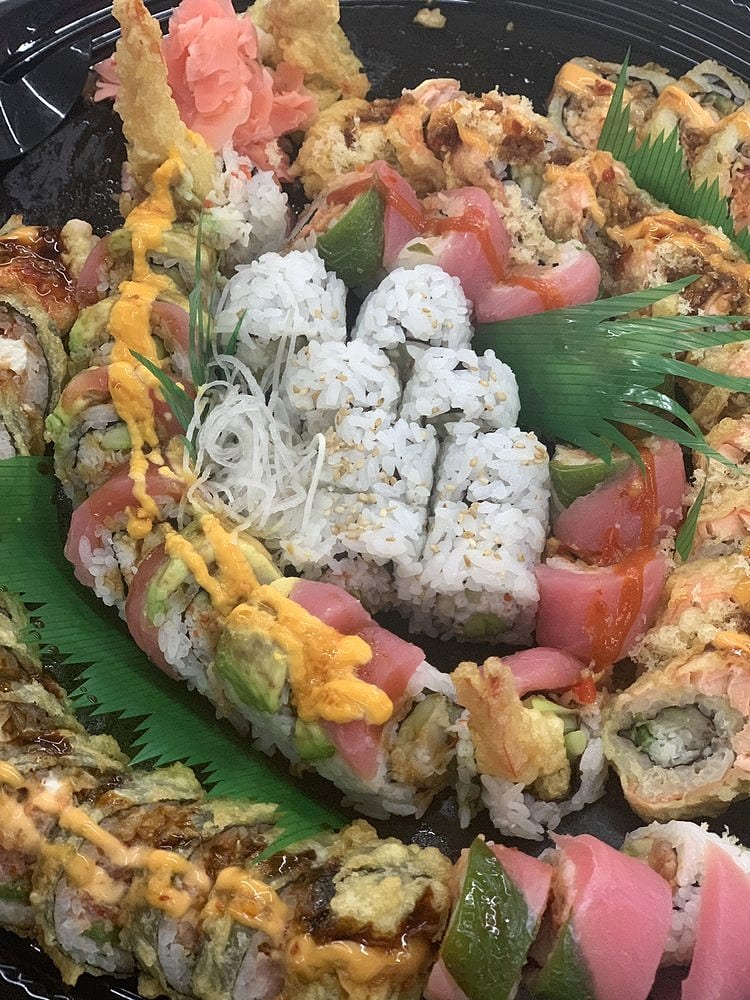 A large party tray of assorted sushi rolls with tuna, avocado, tempura and pickled ginger on leaf garnish